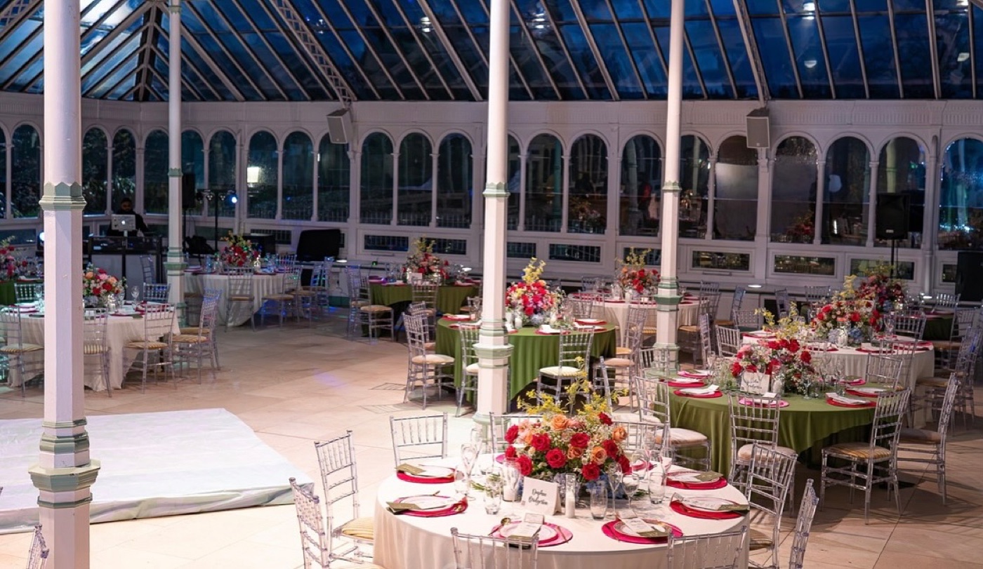 Round tables laid for a gala dinner beneath the glass roof of an orangery