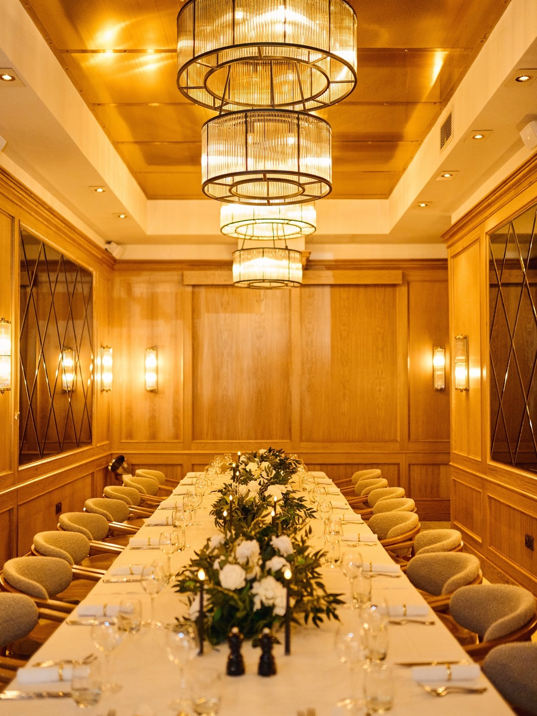 A gilded, wood-panelled private dining room with a single long table beneath tiered chandeliers