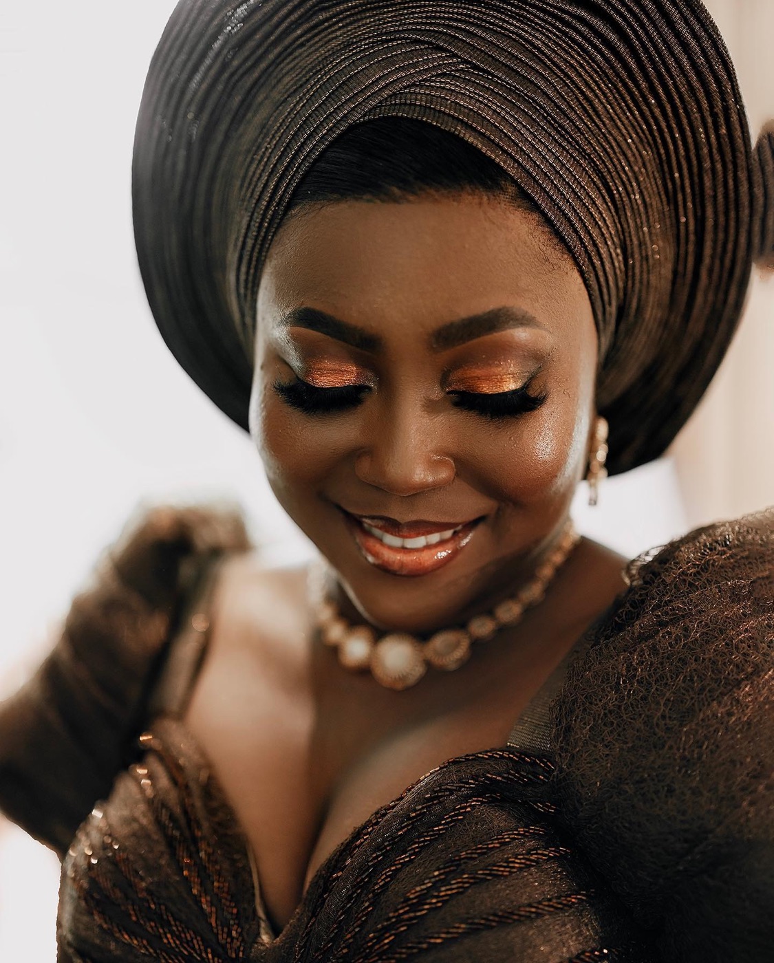 A bride in gold aso-oke, portrait against a plain ground