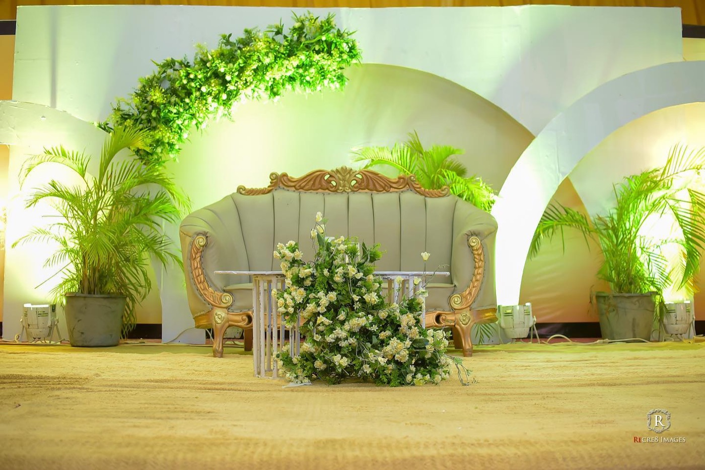 A ceremony stage framed by white arches and banks of green foliage and white florals