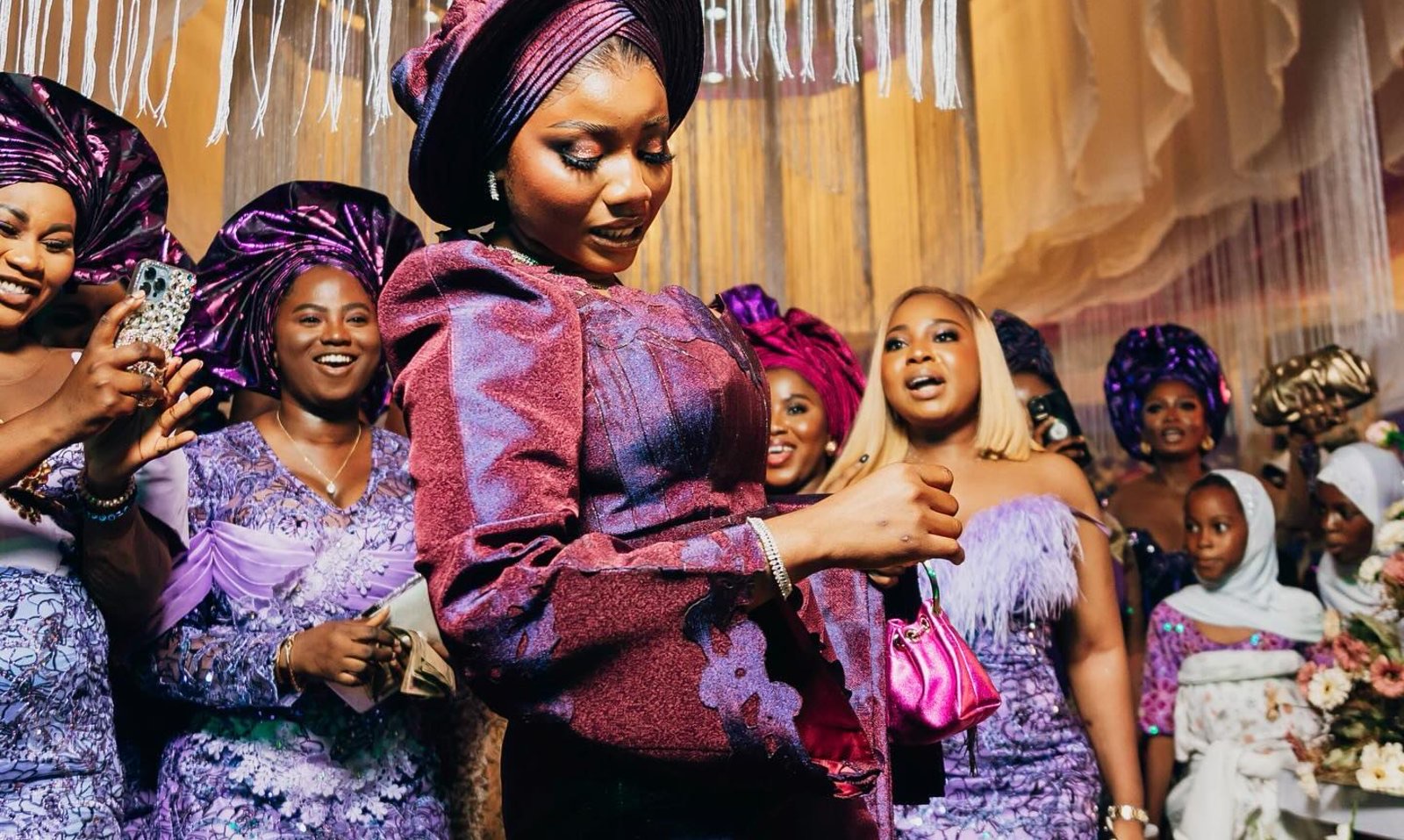 A group of guests in coordinated purple aso-ebi and gele, mid-celebration