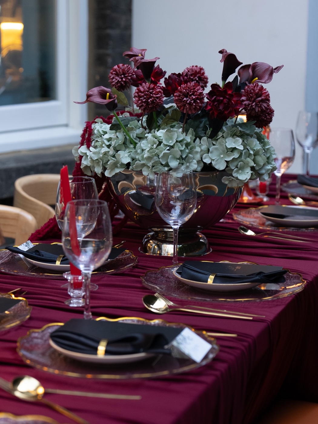 A centrepiece of garnet dahlias, calla lilies and pale hydrangea in a silver bowl