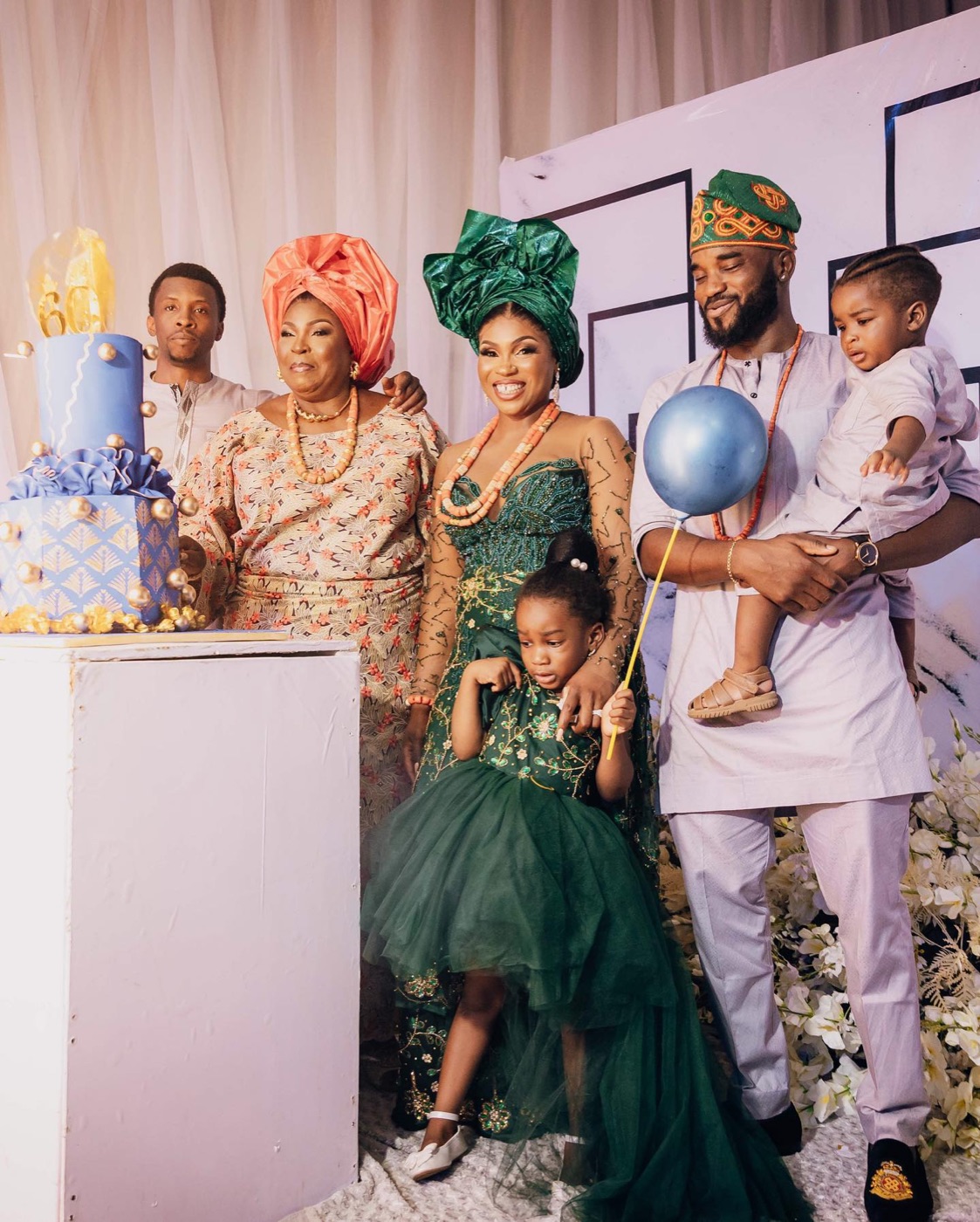 A pastel blue tiered birthday cake with a gold sixty topper, family gathered around