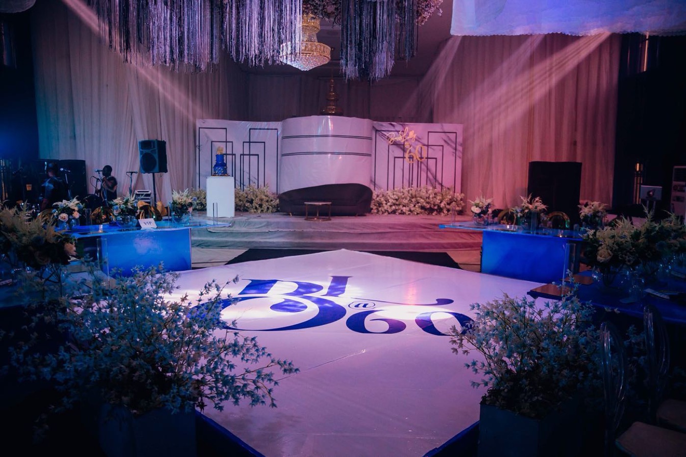 A lit dance floor framed by florals and blue uplighting in a ballroom after dark