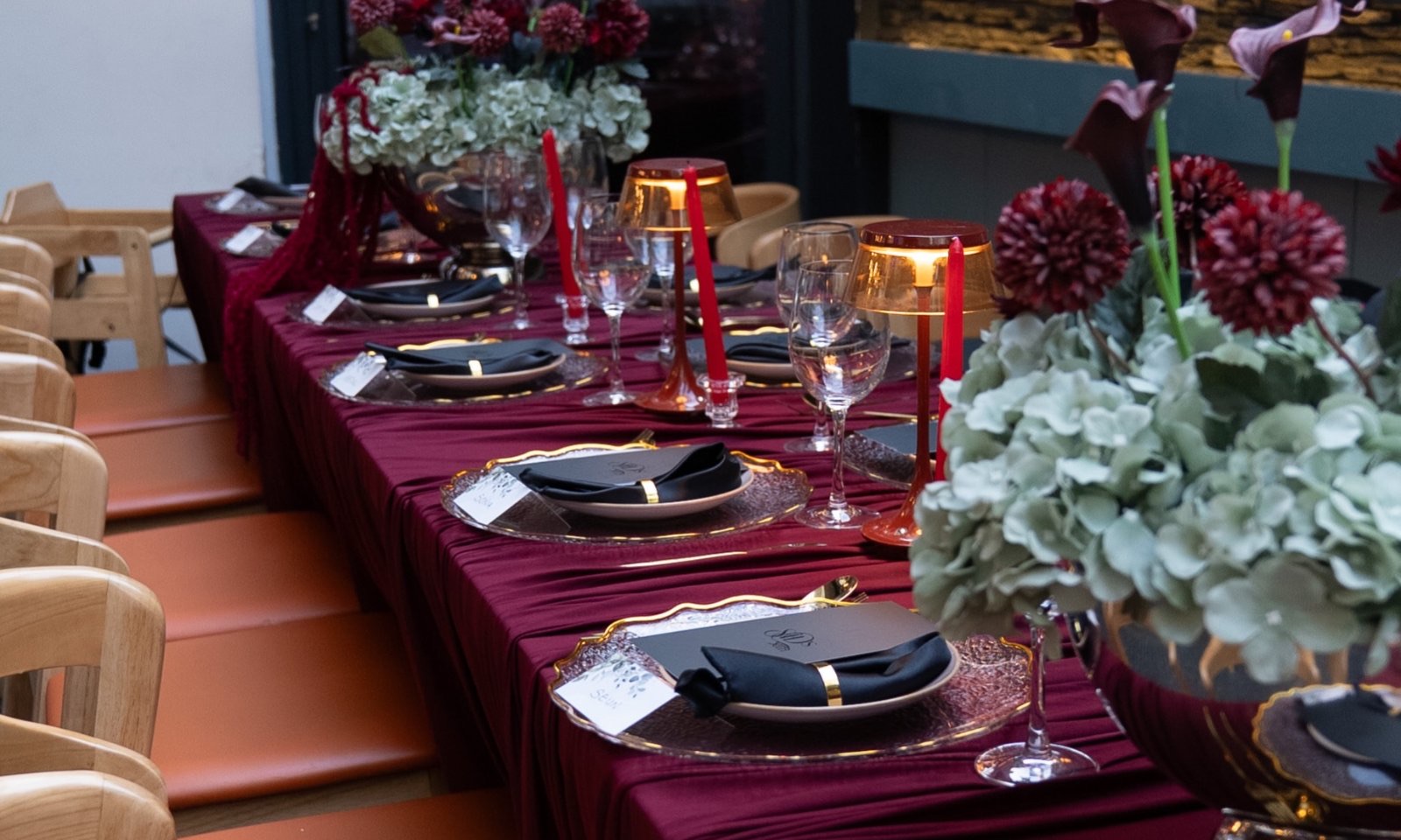 A long banquet table in burgundy and gold running the length of a glass-roofed room