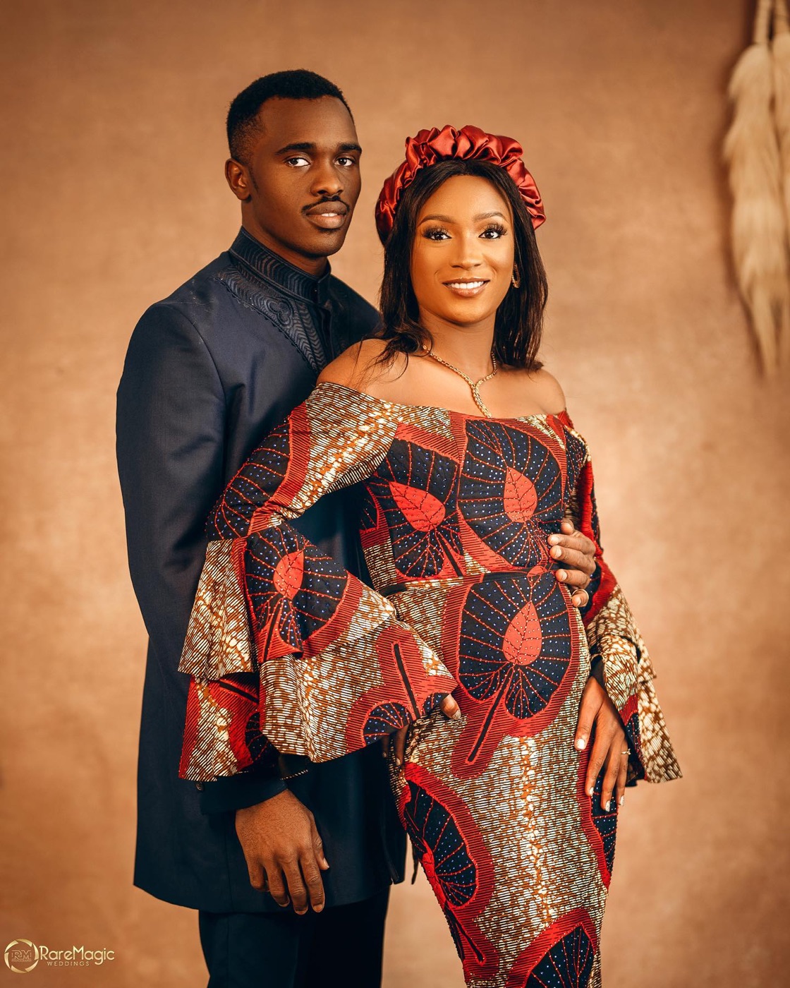 A couple in matching red and gold ankara print, embracing outdoors