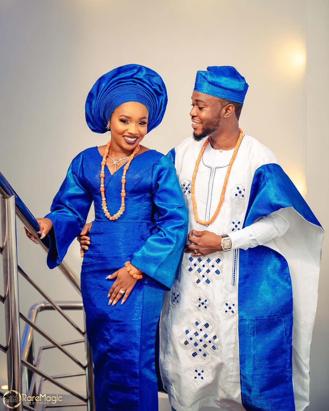 A couple in matching royal blue and white aso-oke, standing on a staircase