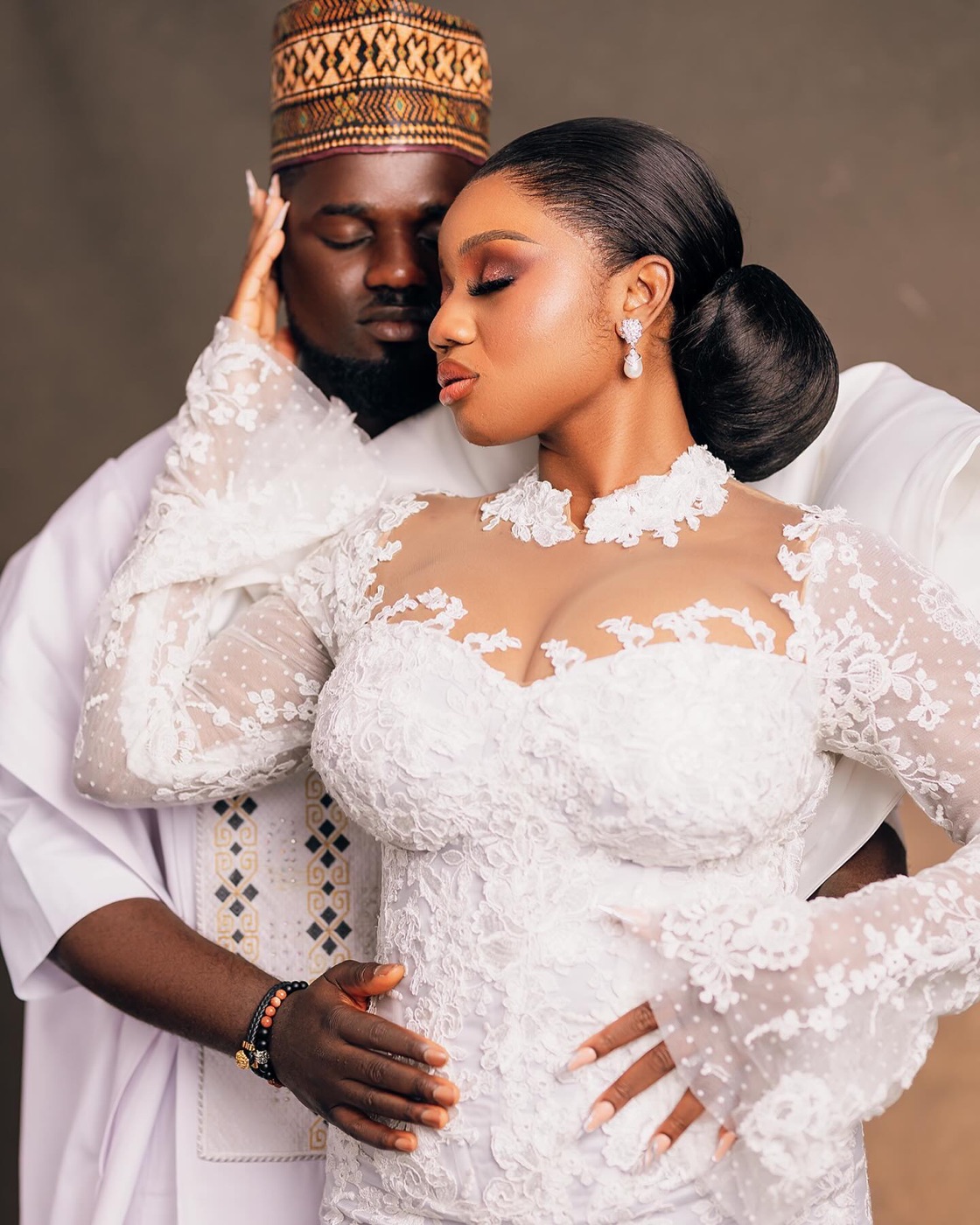 A bride and groom in white lace and gold, photographed close and still