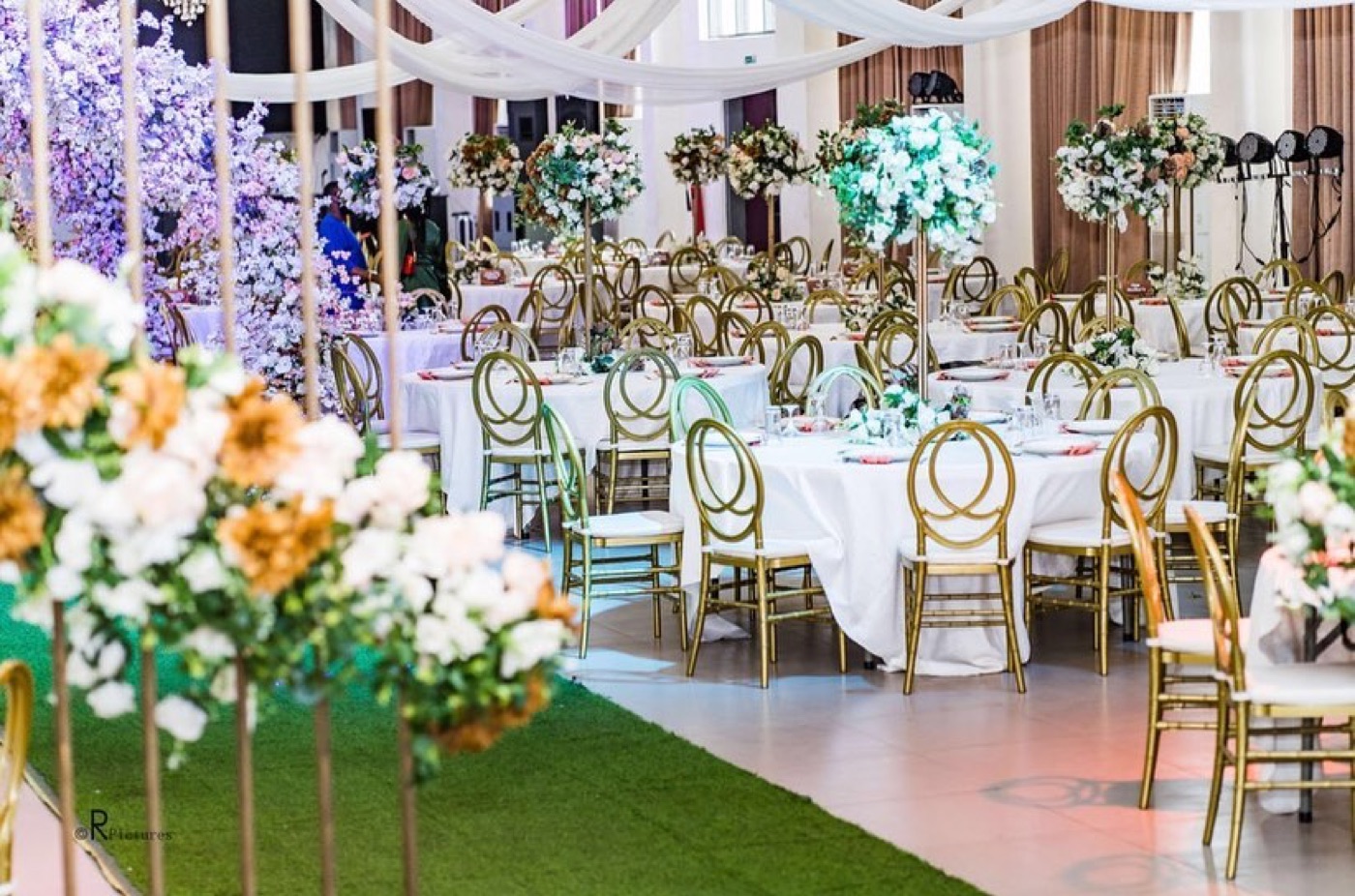 A marquee reception with gold chairs, white linen and tall floral arrangements