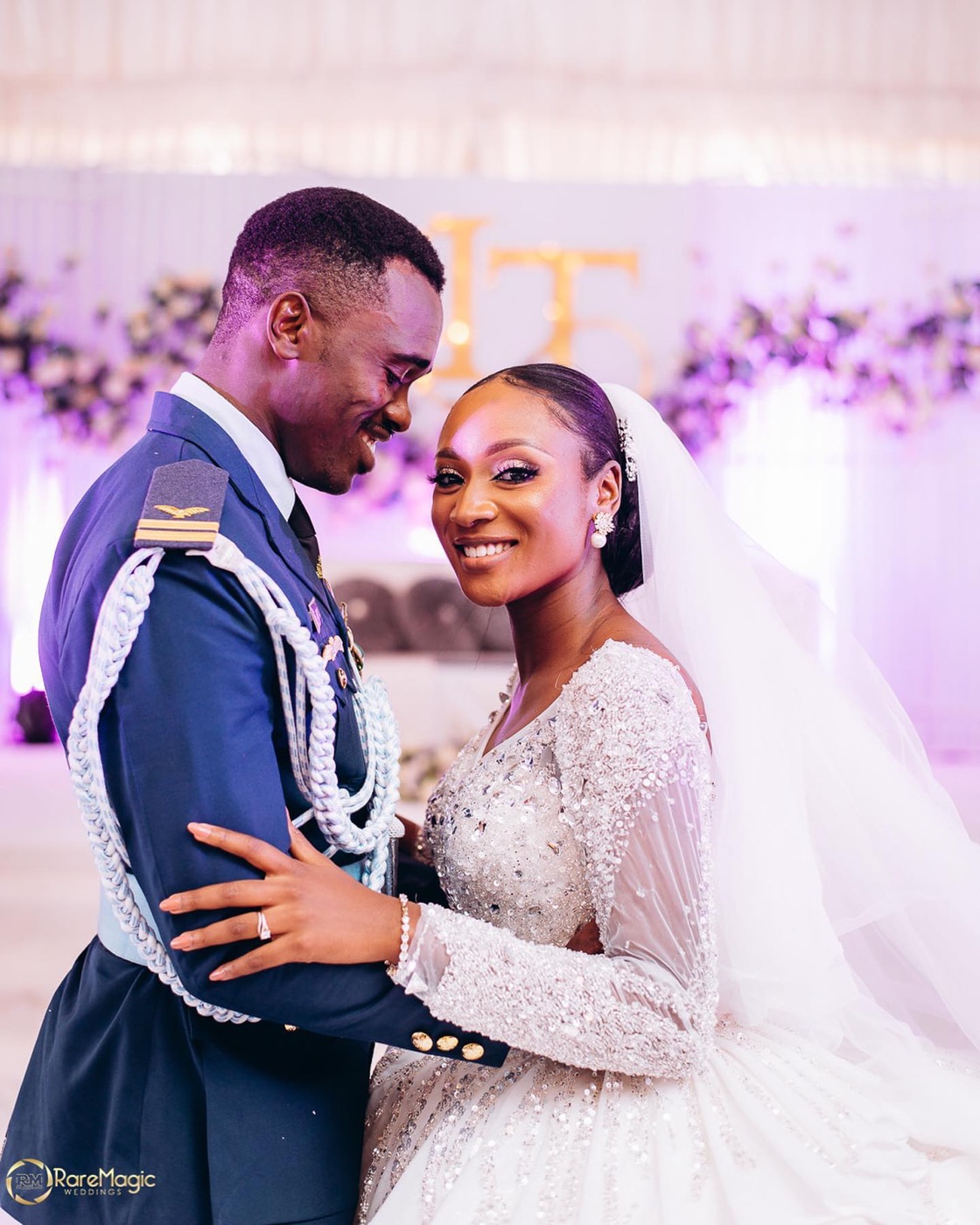 A groom in RAF dress uniform embracing his bride, purple-lit reception behind them